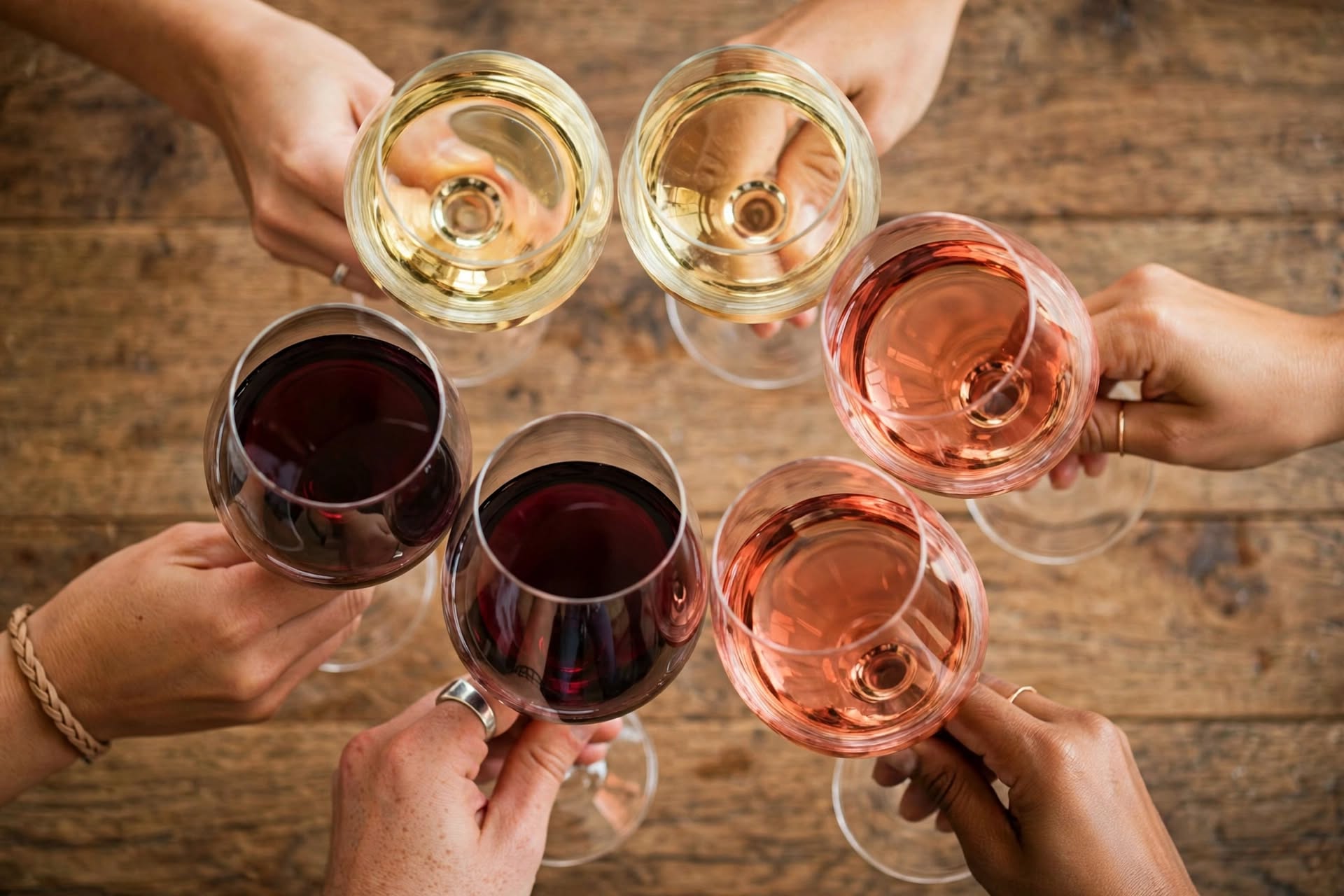 Plusieurs mains trinquant avec des verres de vin rouge, rosé et blanc